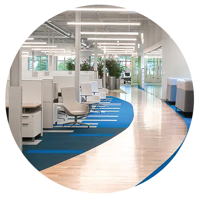 Empty white office with cubicles, partial glass walls, blue carpet and a laminated wood walkway